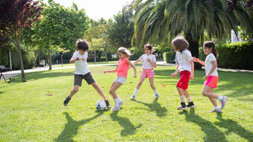 Group of kids enjoying a game of soccer in a lush green park on a sunny day in Portugal.